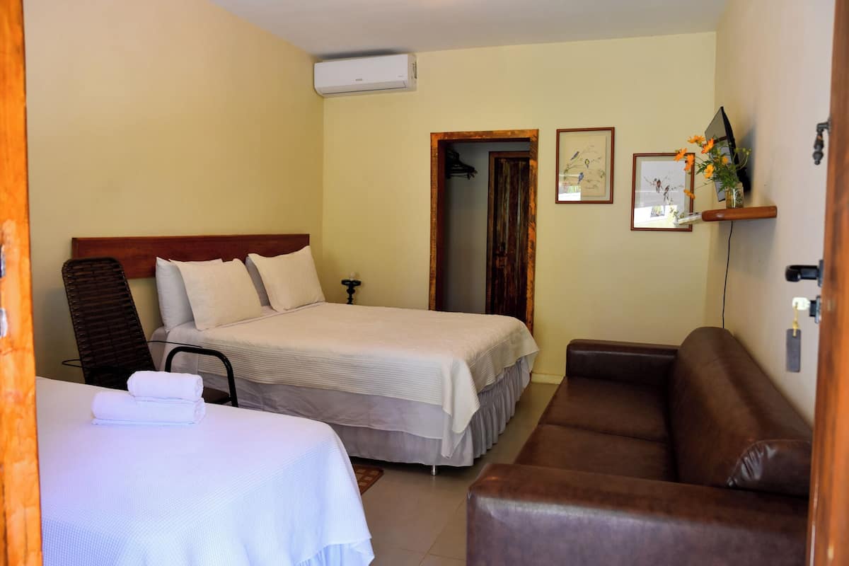Ein Hotelzimmer mit einem Doppelbett, einem braunen Ledersofa, einem Sessel, einem kleinen Tisch und einem Fernseher auf einem Holzständer.