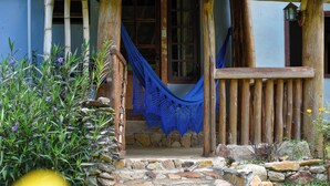 Un porche de madera rústico con una hamaca, escalones de piedra y un muro de piedra.
