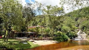 Un entorno ribereño con una estructura de madera, un pequeño puente y una casa al fondo.