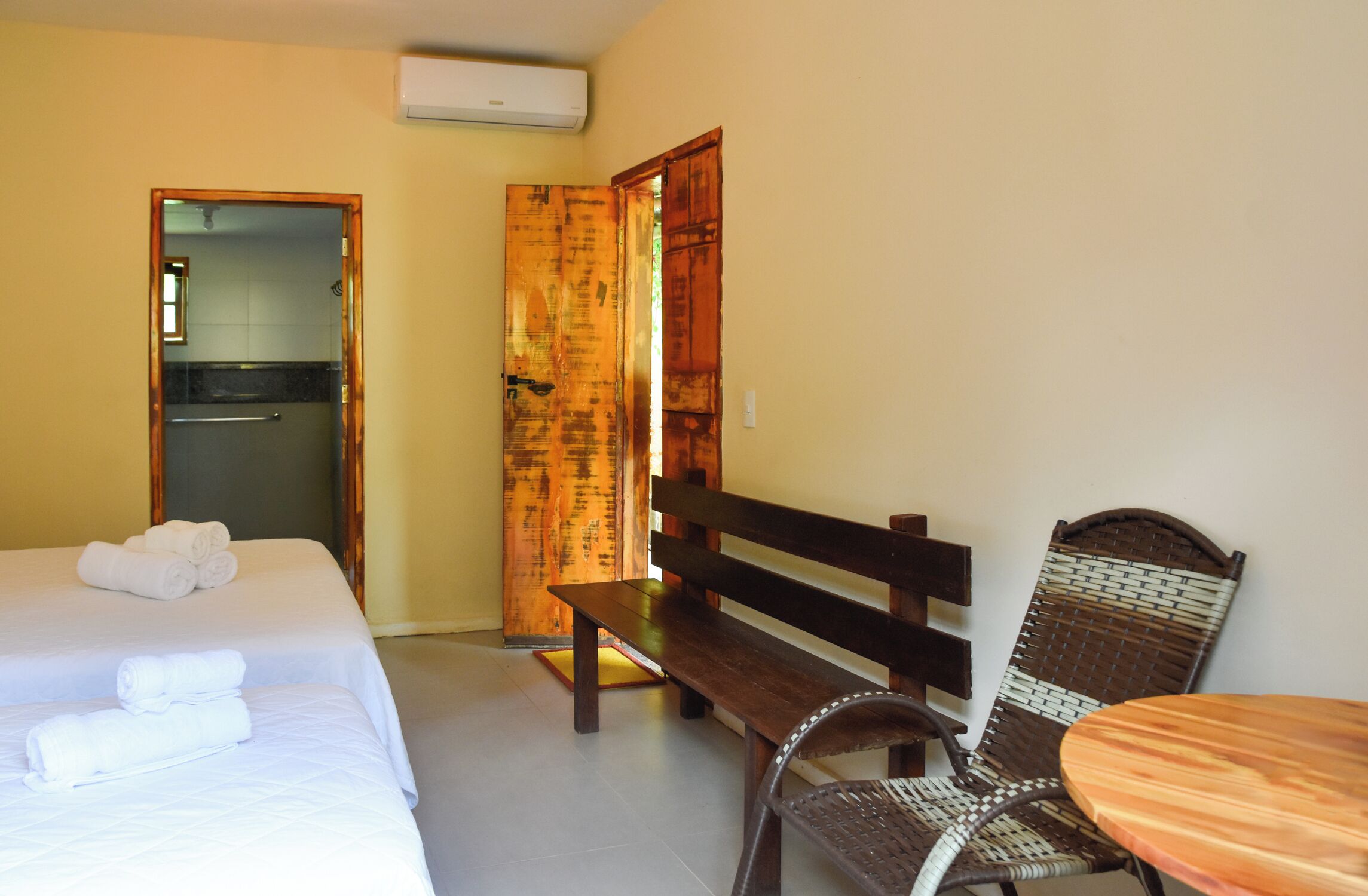 Ein Hotelzimmer mit einem Bett, einer hölzernen Bank, einem Korbsessel und einem kleinen Holztisch.