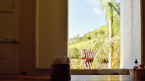 Una habitación con ventana que da a una colina con palmeras y tejas de terracota.