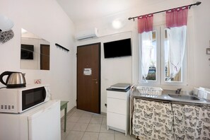 A compact kitchen with a microwave, a small refrigerator, a sink, and a window with curtains.