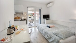 A compact hotel room with a kitchenette, a bed with patterned bedding, a television, and a sliding glass door to the outside. - Holiday Home 'Il Gattino Di Porto Appartamento 4' with Shared Pool, Wi-Fi and Air Conditioning (Imperia)