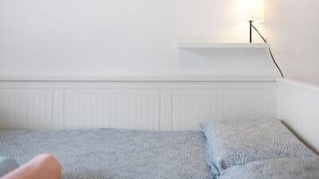 Een witte kamer met een bed, een witte plank en een wandlamp.