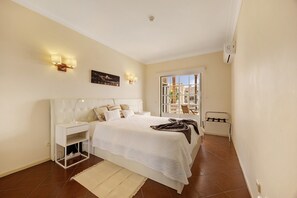 A bedroom with a bed, bedside tables, a nightstand, a window with a view, and a balcony. - Apartment 'Sol Do Atlântico' with Shared Pool, Wi-Fi and Air Conditioning (Portimão)