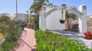 Um arco branco com a inscrição 'Laguna Beach', um vaso pendurado e um caminho que leva à praia.