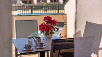 Un balcón con una mesa lista para dos personas, un florero y vistas a edificios al fondo.