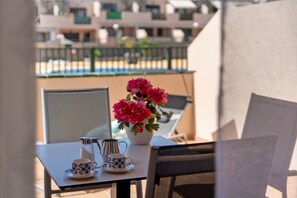 A balcony with a table set for two, a flower vase, and a view of buildings in the background. - Vacation Apartment 'Apartamento Los Geranios' with Shared Pool, Private Terrace and Wi-Fi (Arona)