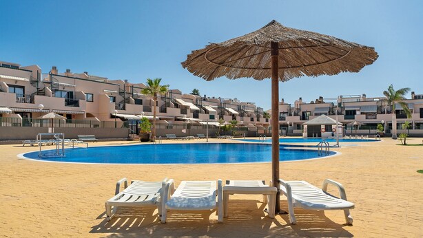 A swimming pool with lounge chairs and a thatched umbrella, surrounded by buildings. - Vacation Apartment 'Apartamento Los Geranios' with Shared Pool, Private Terrace and Wi-Fi (Arona)