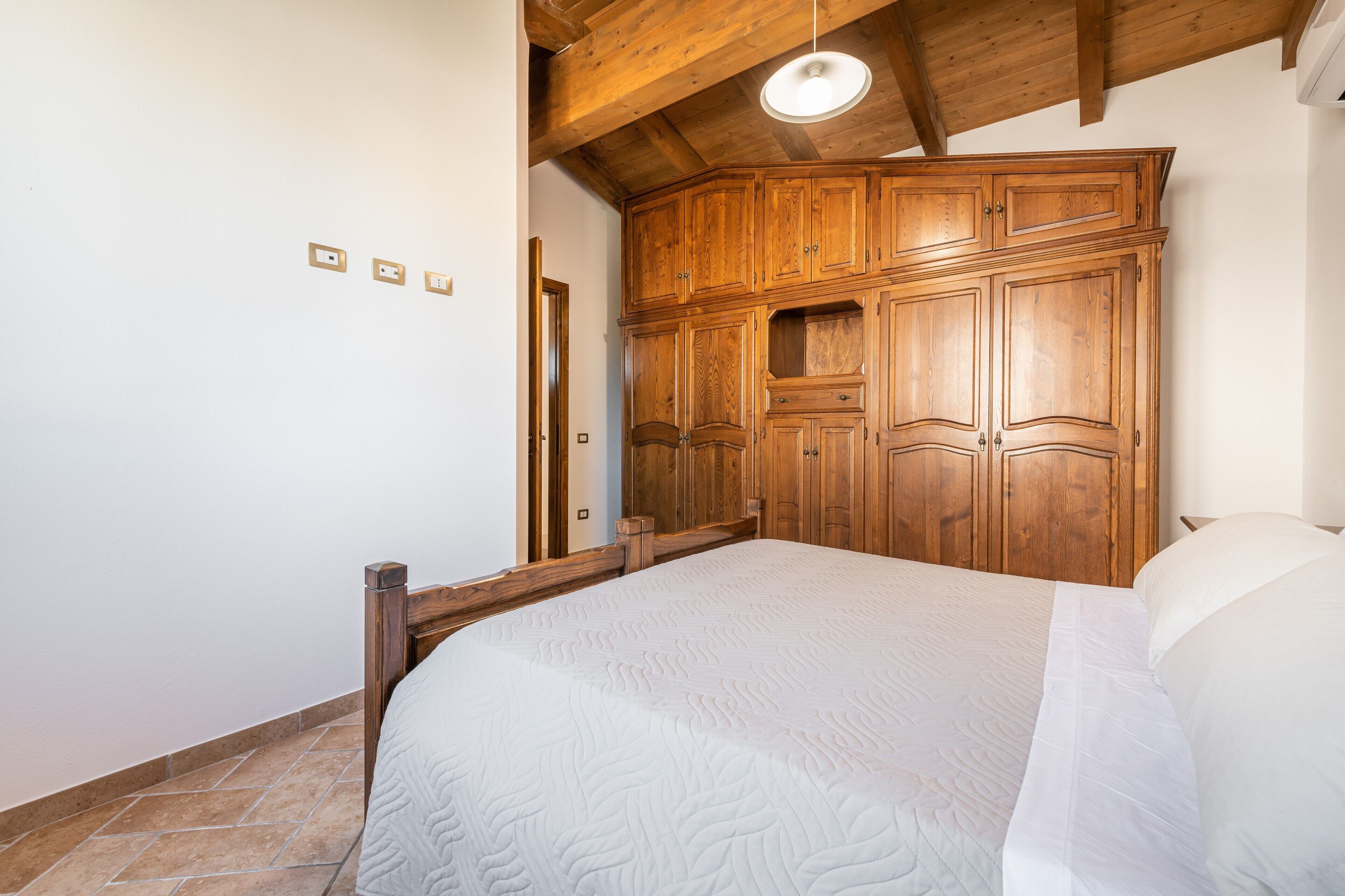 Ein Schlafzimmer mit einem Holzschrank, einem Bett mit weißer Bettwäsche und einem gefliesten Boden.