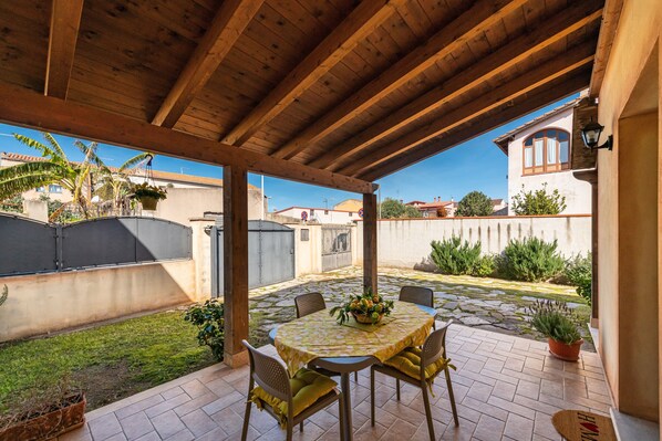 A covered patio with a round table and chairs, a potted plant, and a view of the surrounding area.