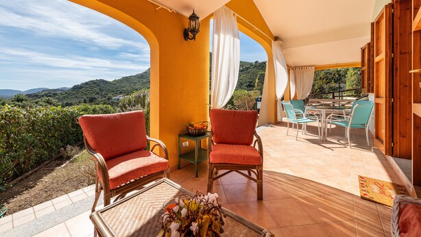A terrace with wicker chairs, a table, and a view of the hills. - Holiday Home 'Domixedda' with Sea View, Private Terrace and Air Conditioning (Costa Rei)