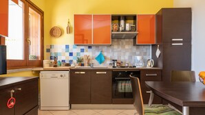 A kitchen with brown cabinets, a dishwasher, a tiled backsplash, and a dining area with a table and chairs. - Holiday Home 'Domixedda' with Sea View, Private Terrace and Air Conditioning (Costa Rei)