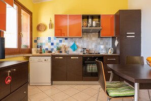 A kitchen with brown cabinets, a dishwasher, a tiled backsplash, and a dining area with a table and chairs. - Holiday Home 'Domixedda' with Sea View, Private Terrace and Air Conditioning (Costa Rei)