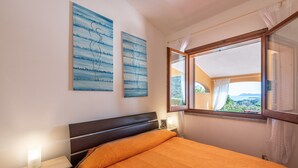 A bedroom with a bed, a nightstand, a lamp, a window with a view, and two wall art pieces. - Holiday Home 'Domixedda' with Sea View, Private Terrace and Air Conditioning (Costa Rei)
