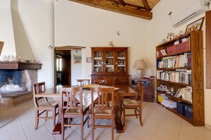 Un comedor con una mesa y sillas de madera, una chimenea, una estantería y una zona de cocina.