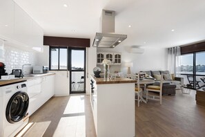 A modern kitchen with a built-in washer, a dining area with a view, and a living space with a sofa and a table.
