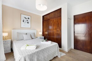 A bedroom with a bed, a wooden wardrobe, a nightstand with a lamp, and a framed picture on the wall.