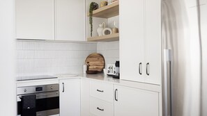 A modern kitchen with white cabinetry, a stainless steel oven, a wooden cutting board, and a coffee maker.