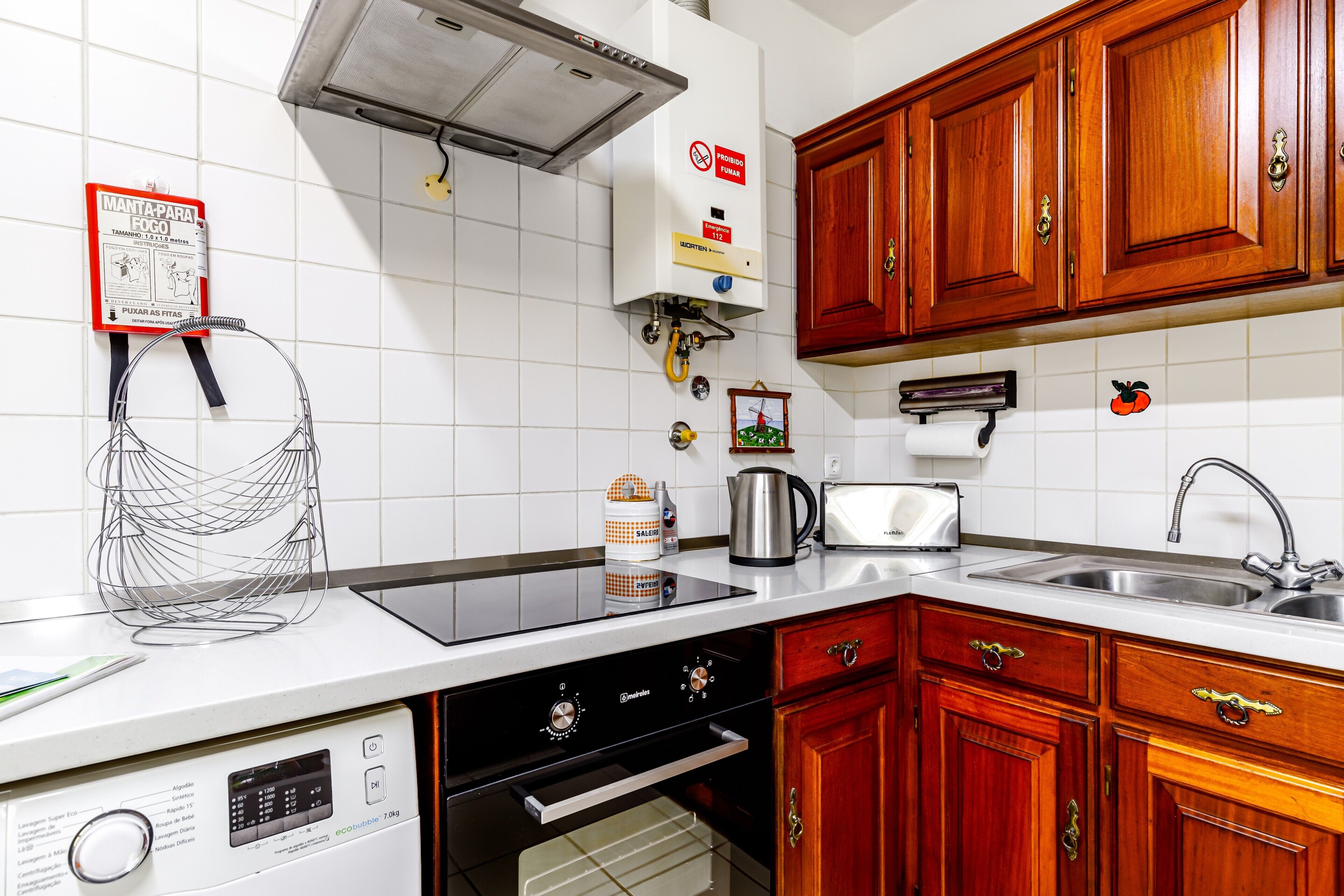 A kitchen with white tiles, wooden cabinets, a stainless steel sink, a built-in oven, and a dishwasher.
