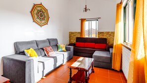 Un salon avec un canapé gris, un canapé rouge et noir, une table basse en verre et un élément décoratif géométrique sur le mur.