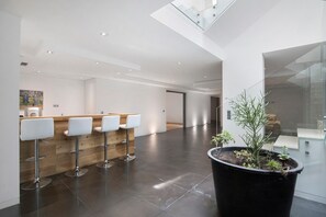 Un interior moderno con mostrador de recepción, taburetes de bar y una planta en maceta.