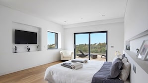 Ein modernes Schlafzimmer mit einem großen Bett, einem Flachbildfernseher, einem weißen Stuhl und einem Balkon mit Blick.