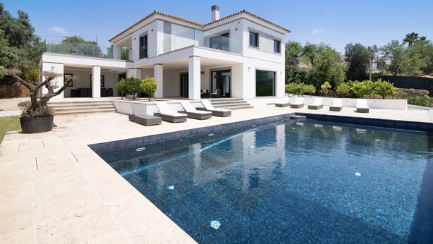 Ein modernes, zweistöckiges Haus mit Swimmingpool, Sitzgelegenheit im Freien und blauem Himmel.