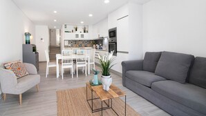 Una sala de estar moderna con un sofá gris, una mesa de centro de madera y un comedor con mobiliario blanco.