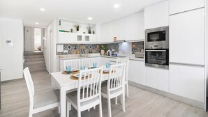 Una cocina moderna con armarios blancos, microondas integrado y una zona de comedor con mesa y sillas blancas.