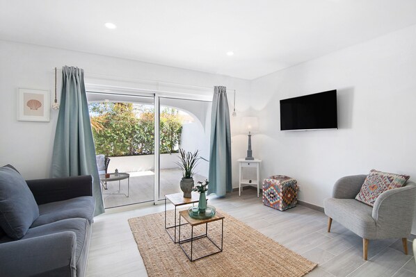 Un salon comprenant un canapé, un fauteuil, un téléviseur à écran plat et une petite table sur laquelle est posé un vase.