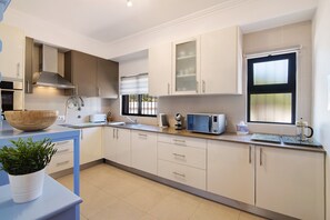 A modern kitchen with white cabinets, a stainless steel range hood, a microwave, and a window with blinds.