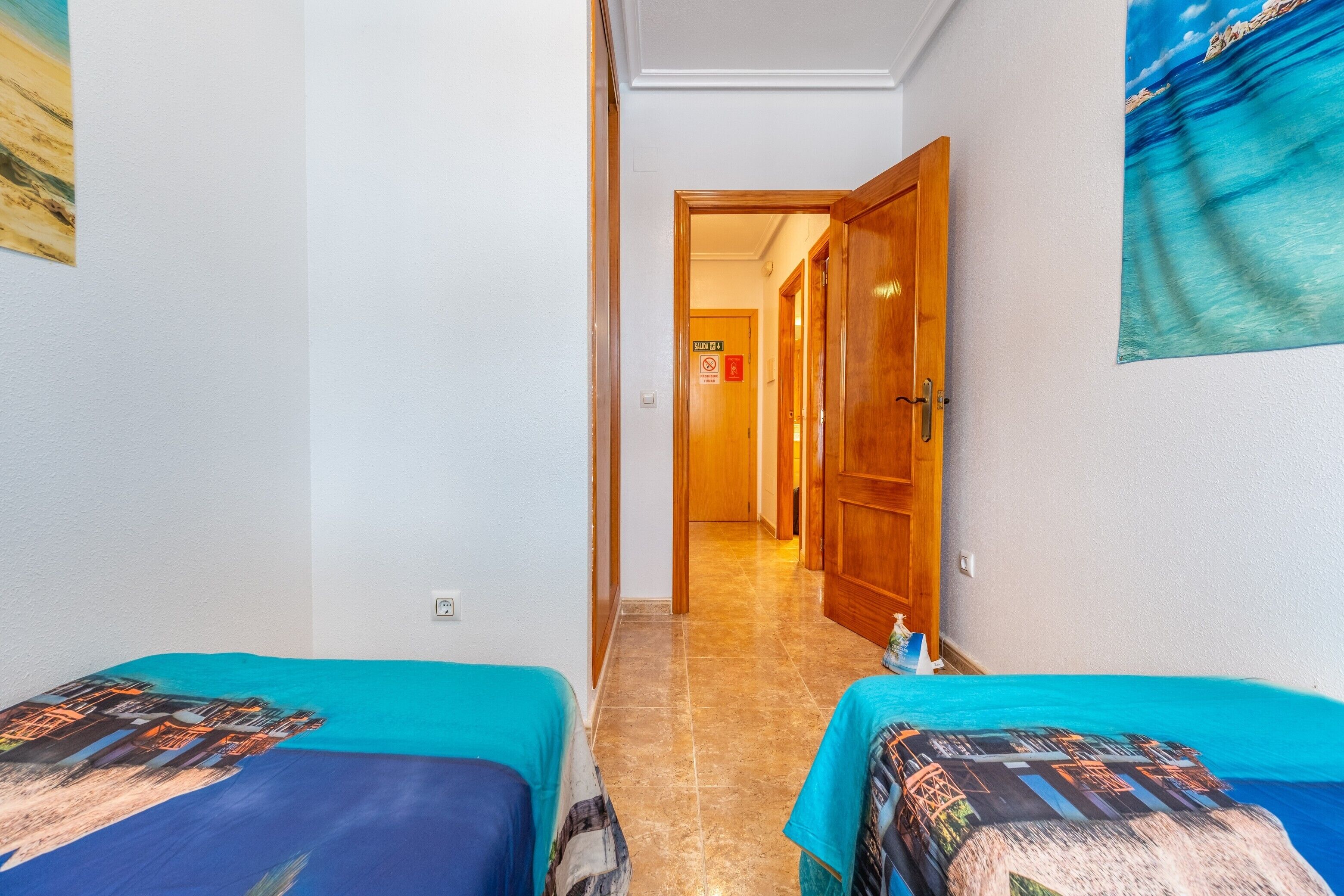 Een hotelkamer met twee bedden, een gang naar een deur en een decoratie aan de muur met een strandthema.