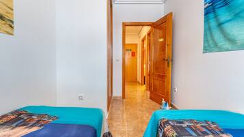 Een hotelkamer met twee bedden, een gang naar een deur en een decoratie aan de muur met een strandthema.