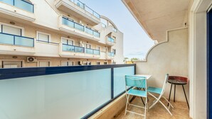 A balcony with a table and chairs, a view of a multi-story building with balconies, and a clear sky.