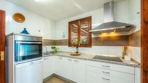 Eine Küche mit weißen Schränken, einem eingebauten Backofen, einer Edelstahl-Dunstabzugshaube und einem Fenster mit Holzrahmen.
