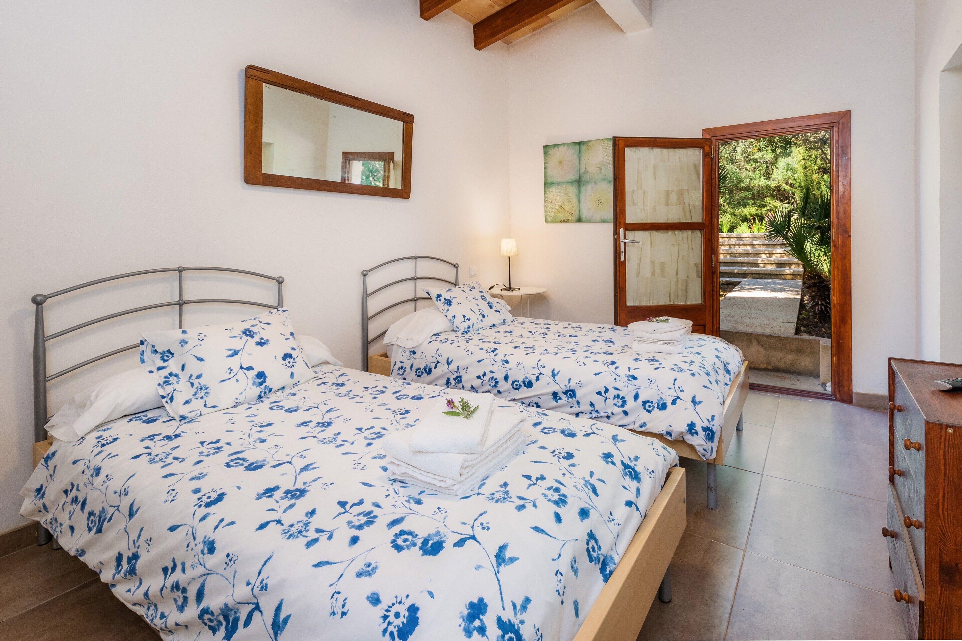 Une chambre avec deux lits, une commode en bois, un miroir et une porte donnant sur un jardin.