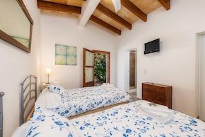 Een slaapkamer met twee bedden, een houten dressoir, een televisie en een raam met uitzicht op groen.