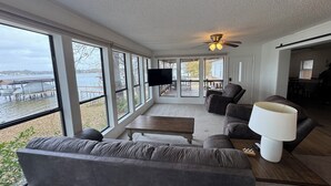 A spacious living room with a large window overlooking a body of water, a ceiling fan, and a flat-screen TV mounted on the wall. - Lakefront with Private Dock & Sandy Shore (Malakoff)