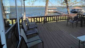A wooden deck with chairs and a table, overlooking a body of water with docks and boats. - Lakefront with Private Dock & Sandy Shore (Malakoff)