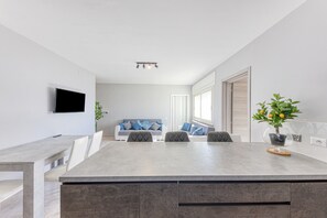 Une cuisine moderne dotée d’un grand îlot central, d’un coin repas avec des chaises, d’un canapé et d’un téléviseur fixé au mur.