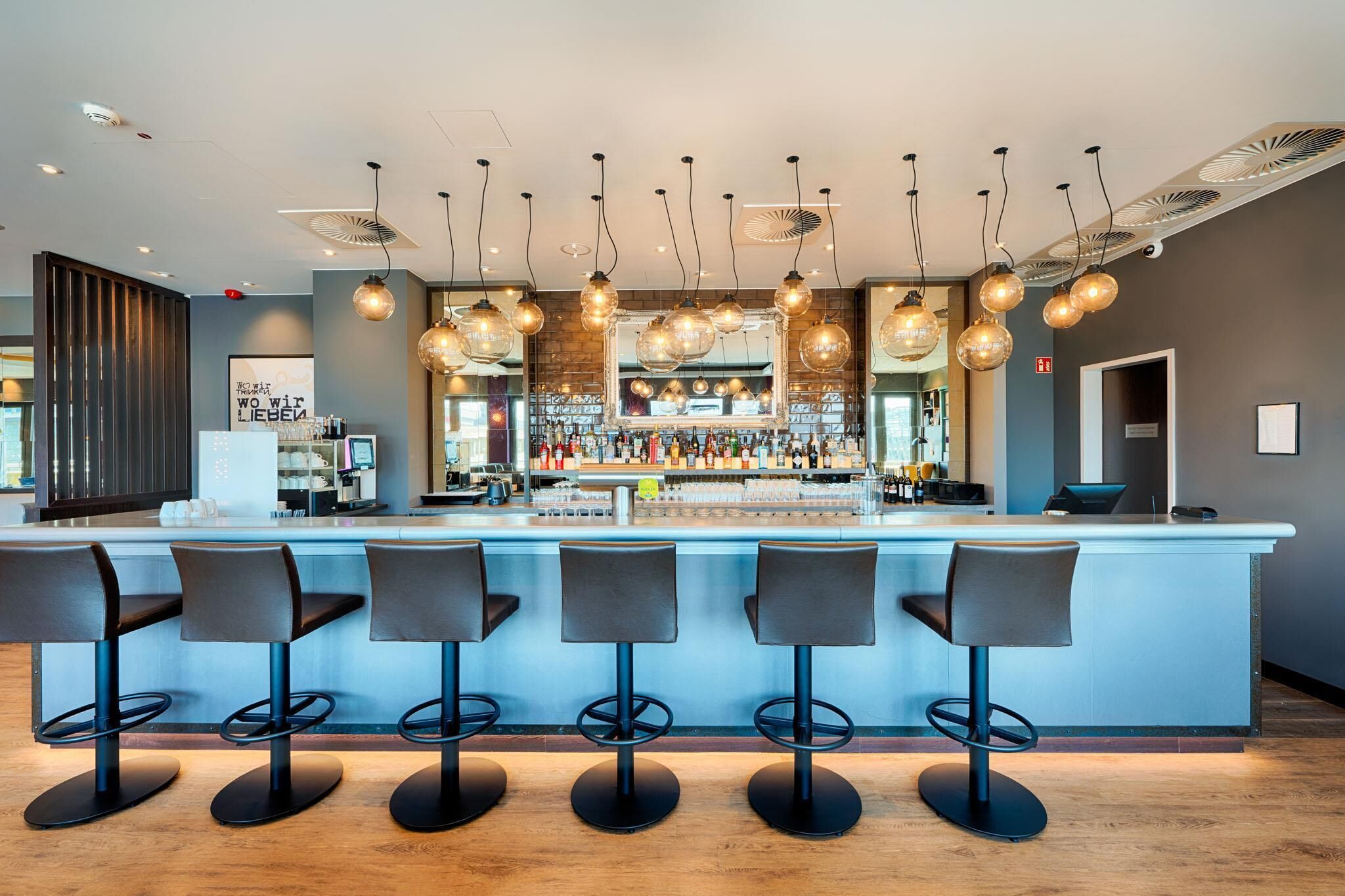 A bar area with a counter, bar stools, hanging light fixtures, and a variety of bottles and glasses.