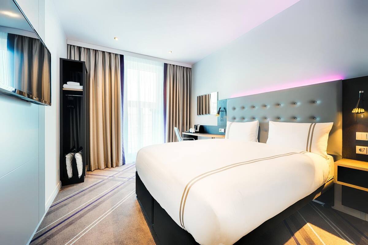 Une chambre d’hôtel moderne équipée d’un grand lit, d’un bureau, d’une armoire et d’un téléviseur.