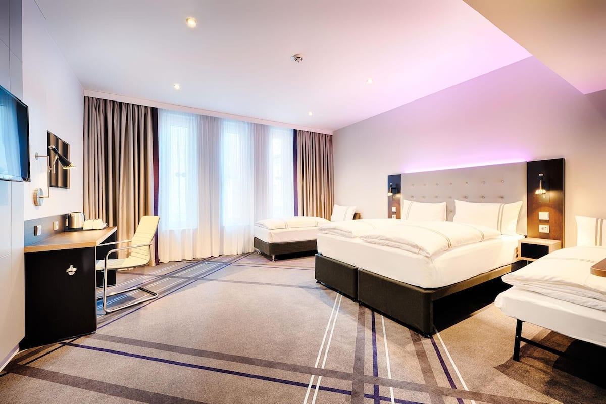 Une chambre d’hôtel avec un lit, un bureau, une chaise et une grande fenêtre avec des rideaux.