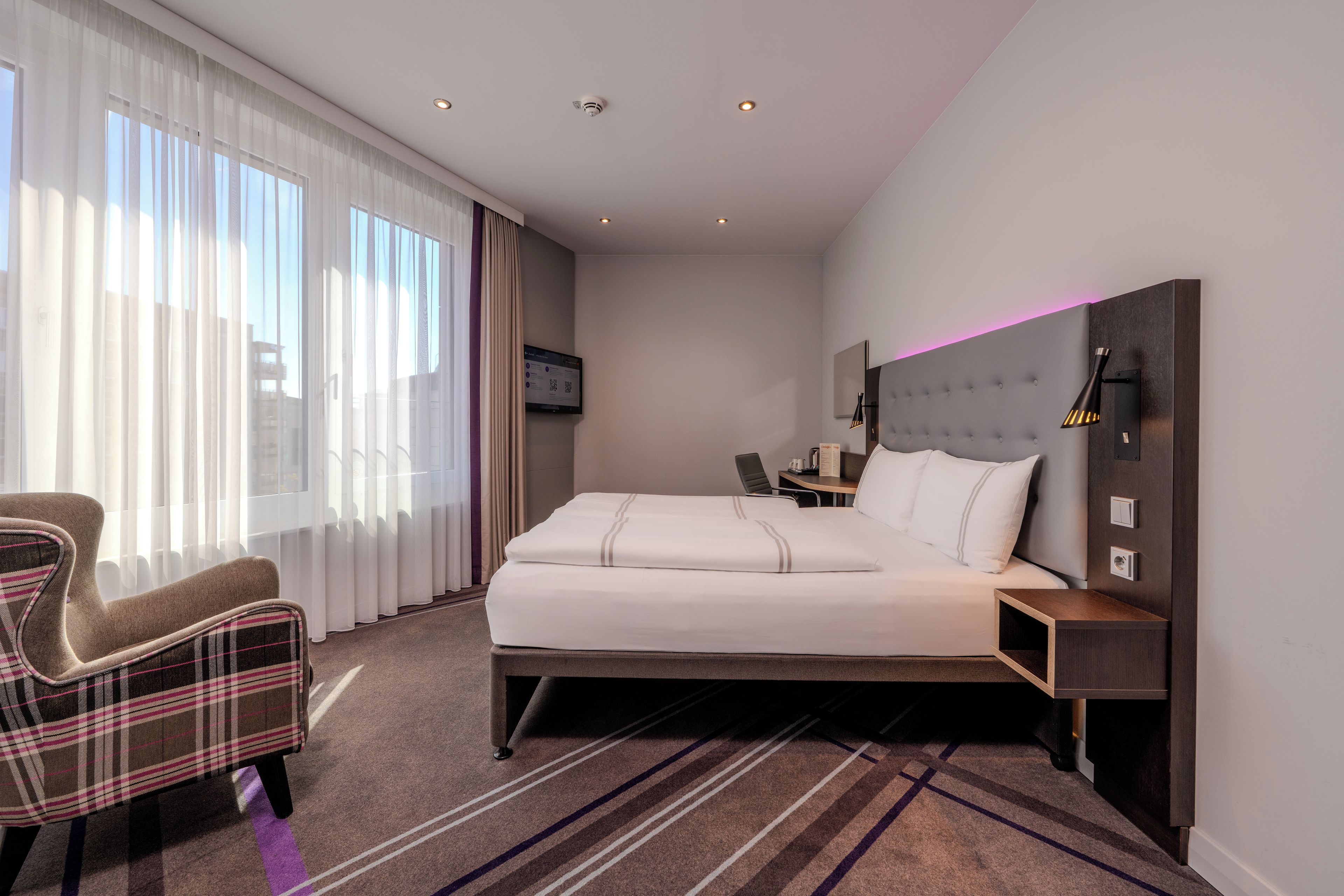 A hotel room with a bed, a chair, a desk, and a television.
