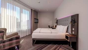 Ein Hotelzimmer mit Bett, Sessel, Schreibtisch und Fernseher.