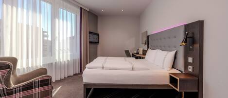 A hotel room with a bed, a chair, a desk, and a television.