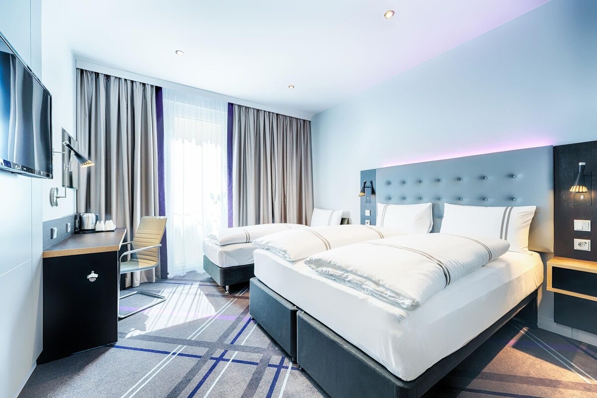 Et moderne hotelværelse med en stor seng, et skrivebord, en stol og et fjernsyn.