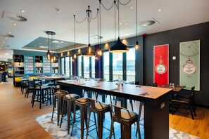 A modern bar area with high tables, hanging pendant lights, and a view of the cityscape. - Premier Inn Dresden City Prager Straße (Dresden)