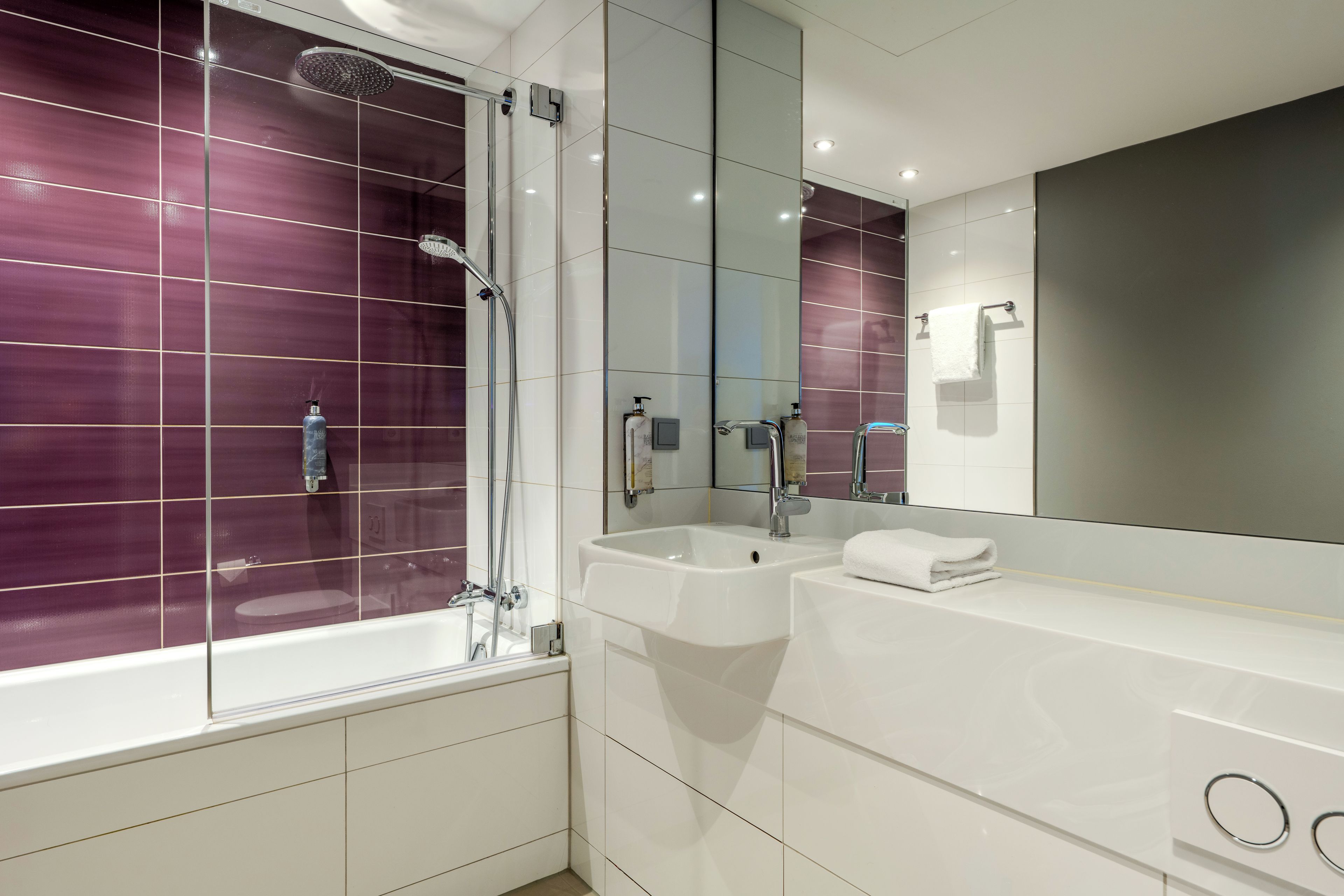 Ein modernes Badezimmer mit einer ein Glas umschlossenen Dusche, einem weißen Waschbecken und einem großen Spiegel.